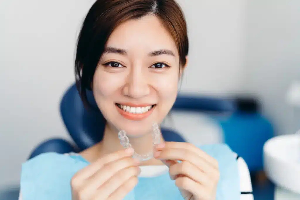 Woman smiling while holding a clear braces aligner at a dental clinic