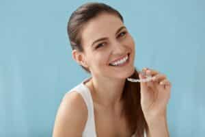 Smiling woman holding clear dental aligners used for teeth straightening treatment.