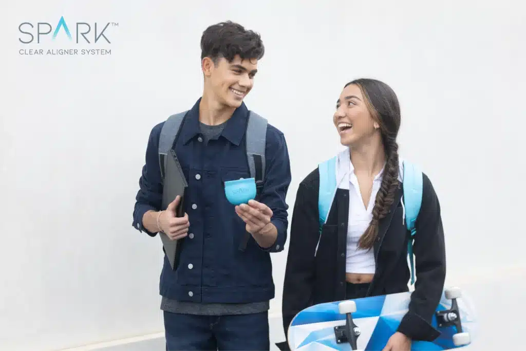 Two active young adults carrying backpacks and a skateboard while holding a Spark aligner case, illustrating how Spark aligners fit into busy, on-the-go lifestyles.